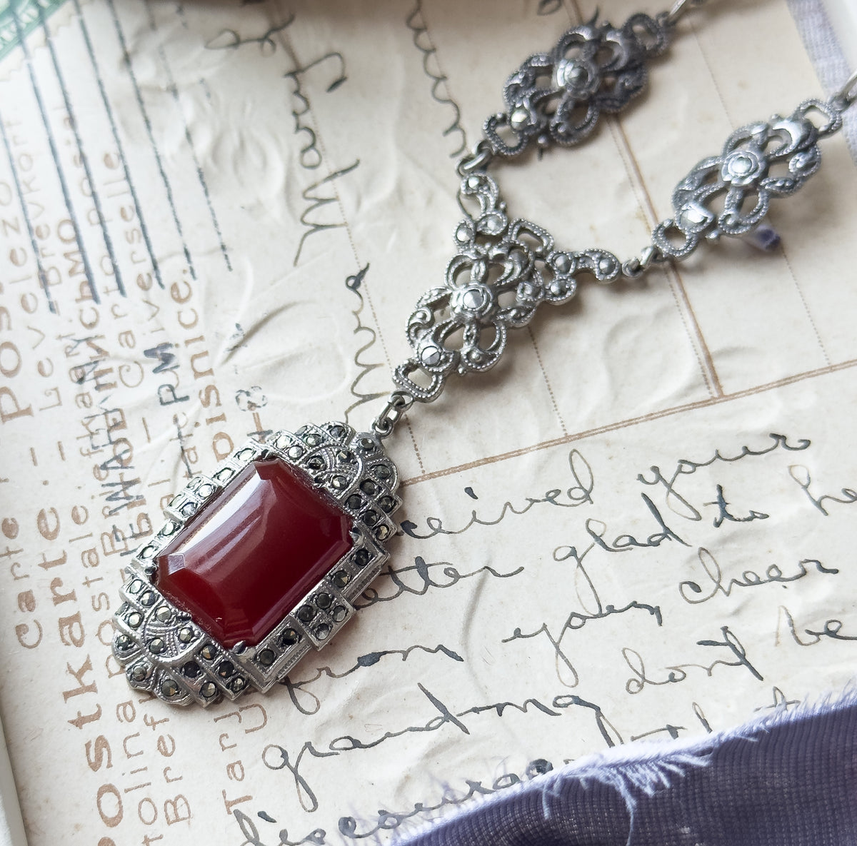 Art Deco carnelian and marcasite necklace in sterling silver, shown laid flat on a handwritten postcard, its rectangular pendant below openwork floral chain stations.