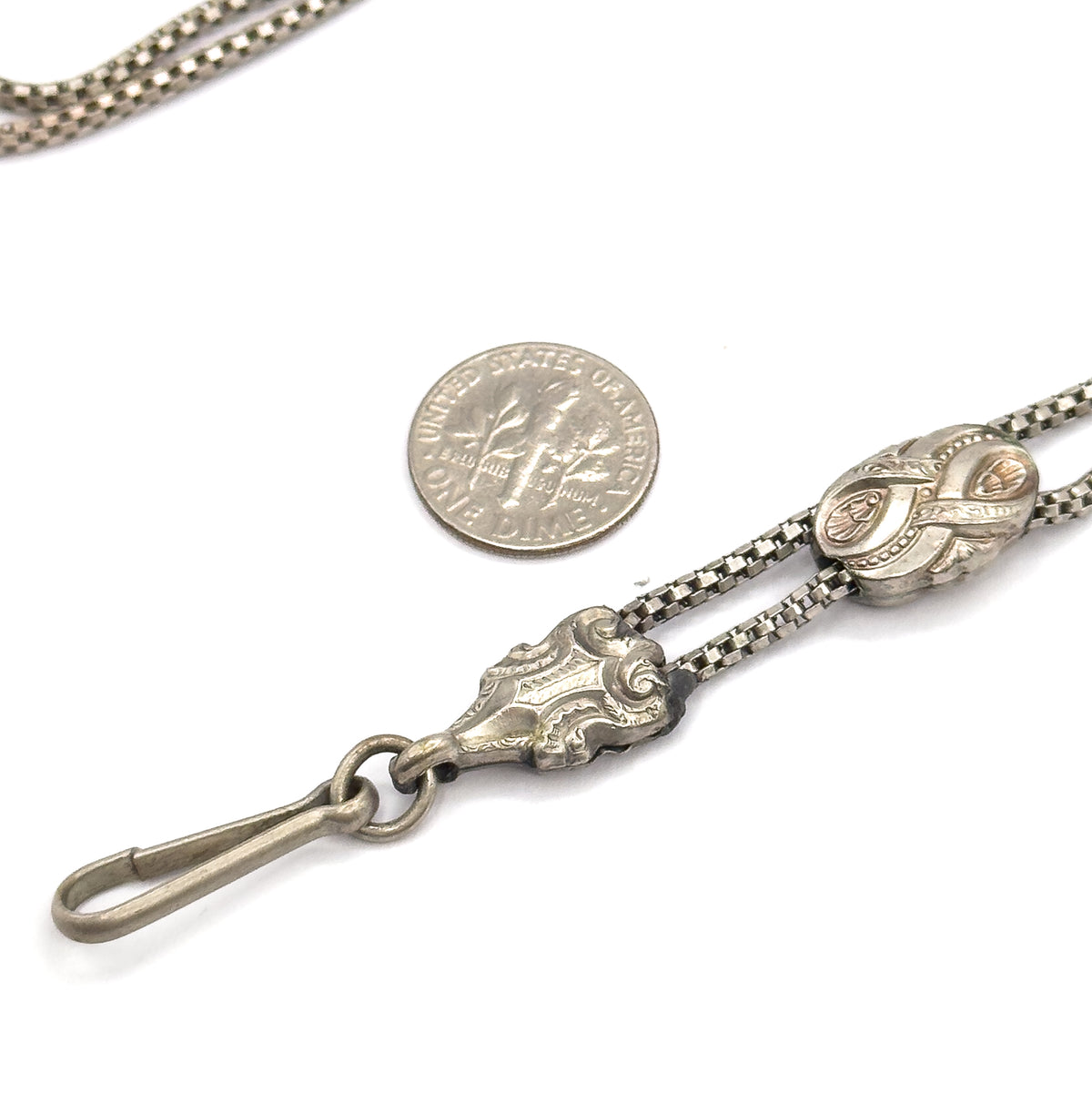 A dime laid beside the chain for scale, with the scrolled fitting, hook clasp and engraved sliding bead spread across the lower right of the frame.