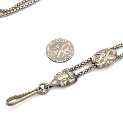 A dime laid beside the chain for scale, with the scrolled fitting, hook clasp and engraved sliding bead spread across the lower right of the frame.