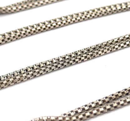 Extreme close-up of the round box chain alone, its square links filling the frame in diagonal lengths against a plain white background.