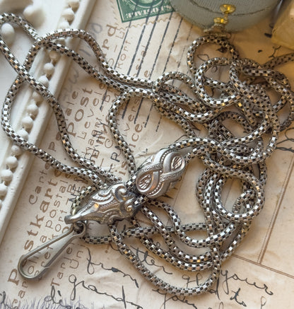 Edwardian base metal watch guard chain, the long round box chain coiled in loops across an old handwritten postcard, with its engraved sliding bead and swivel clasp lying at the centre.