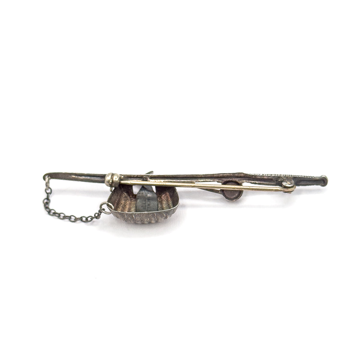 Edge-on view along the length of the brooch, showing how slim the profile is, with the pin stem running beside the pole, the reel bulge mid-bar and the safety chain looping free.