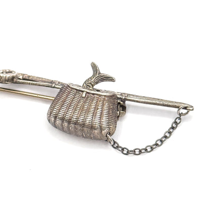 Tight overhead crop on the woven basket, its ribbed texture and darkened patina filling the frame, fish tail rising above the pole and the safety chain trailing down to the lower right.