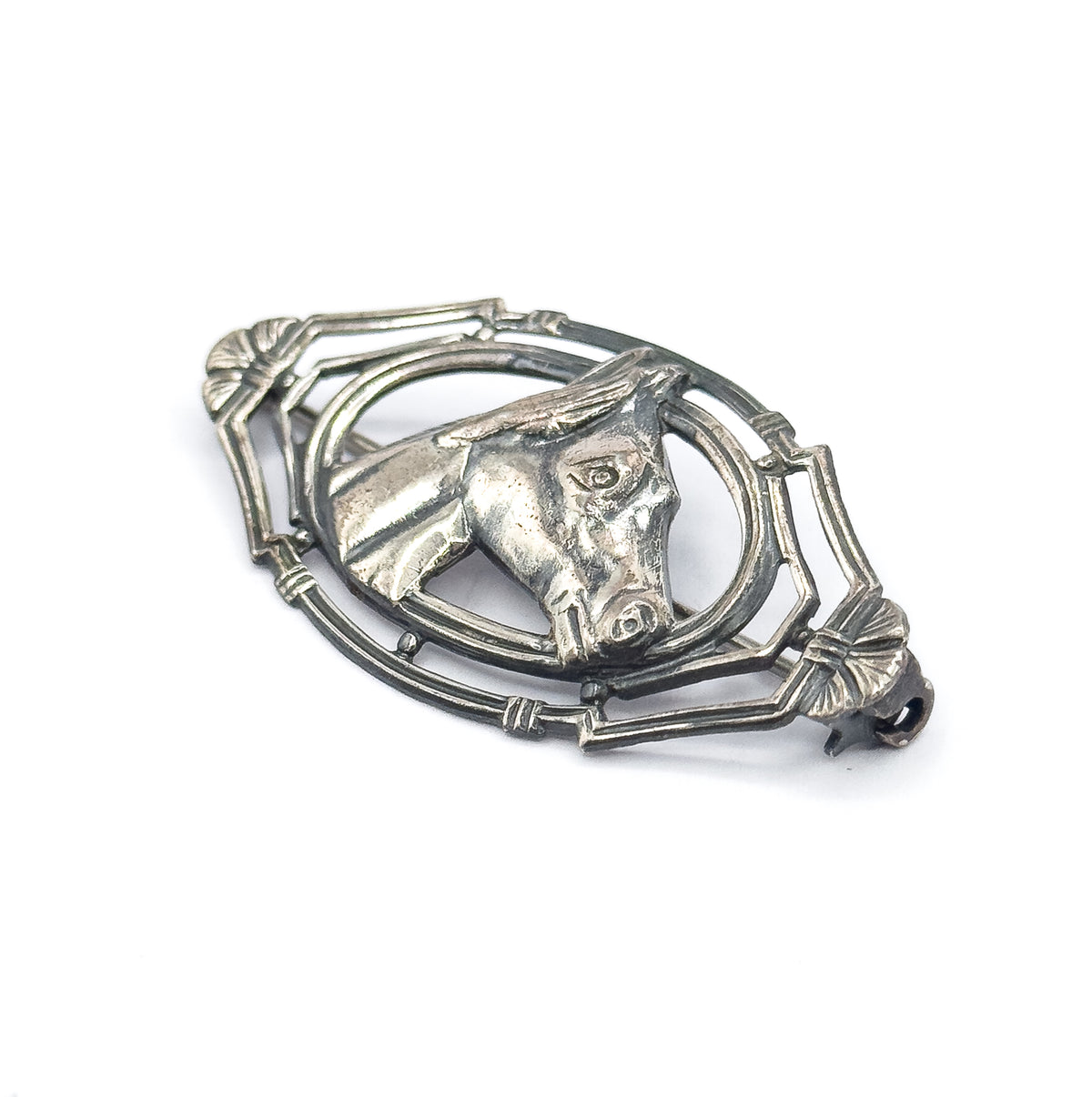 A tilted three-quarter view on white, showing how the horse's head stands proud of the pointed oval frame and the fan-shaped ends, with the pin stem just visible behind.