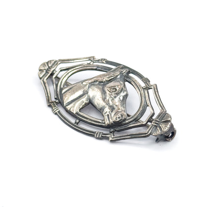 A tilted three-quarter view on white, showing how the horse's head stands proud of the pointed oval frame and the fan-shaped ends, with the pin stem just visible behind.