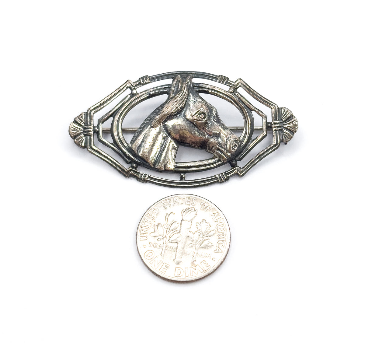 The brooch lies flat beside a dime on white, the coin reaching roughly half the height of the pointed oval frame and giving a clear sense of scale.
