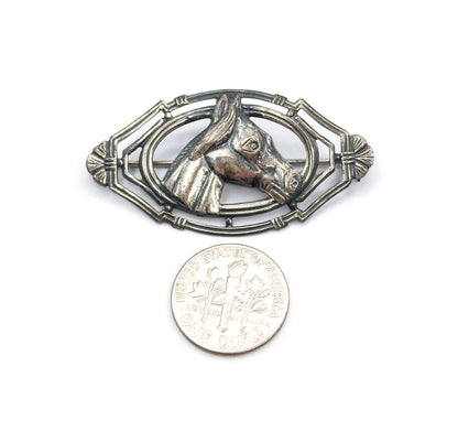 The brooch lies flat beside a dime on white, the coin reaching roughly half the height of the pointed oval frame and giving a clear sense of scale.