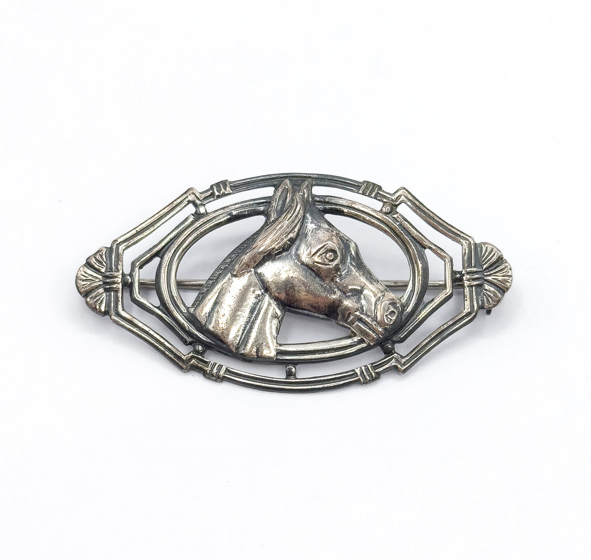 A straight-on front view on white, the horse's head in profile facing right at the centre of the pointed oval openwork frame, with the pin stem visible running behind the bars.