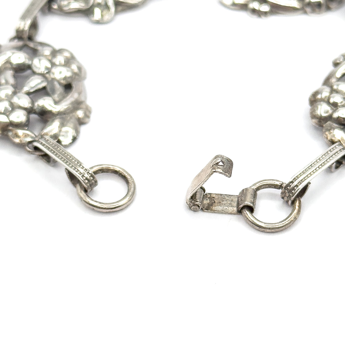 The open clasp fills the frame: a hook on one ribbed bar link facing a round ring on the other, with floral stations curving away at each side.