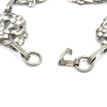 The open clasp fills the frame: a hook on one ribbed bar link facing a round ring on the other, with floral stations curving away at each side.