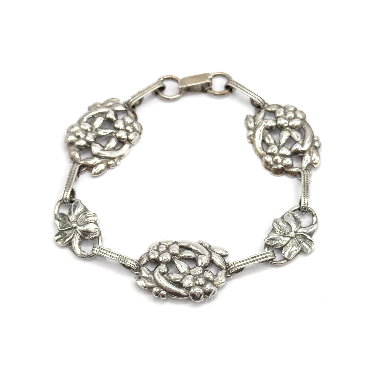 The whole bracelet laid in a full circle on white, clasp closed at the top, showing all five floral stations and the ribbed bars joining them.