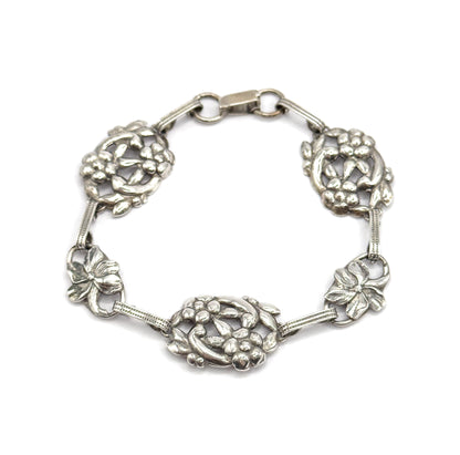 The whole bracelet laid in a full circle on white, clasp closed at the top, showing all five floral stations and the ribbed bars joining them.