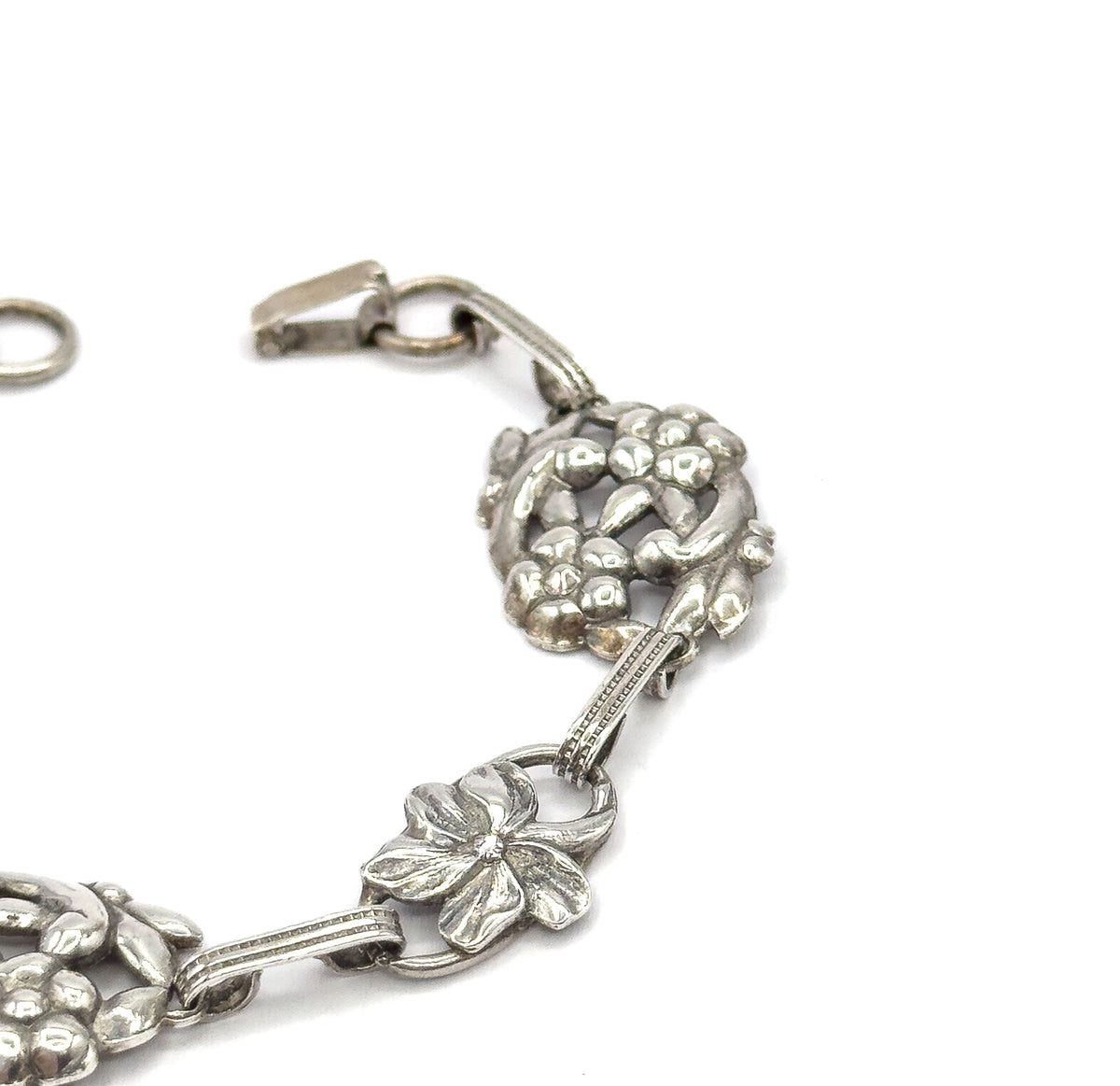 Angled close-up of the unfastened clasp end, hook and round ring apart at the top, beside a domed clustered station and a flatter five-petal flower link below.
