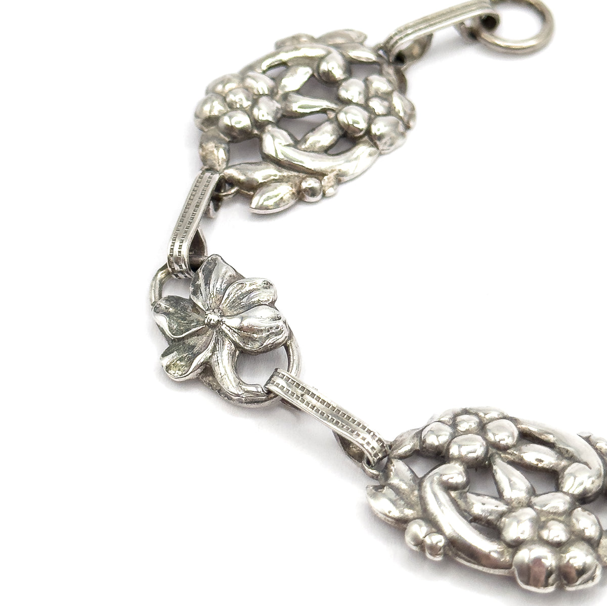 Close overhead view of the middle of the chain, a five-petal flower link set between two ribbed bars with clustered floral stations above and below, patina in the recesses.