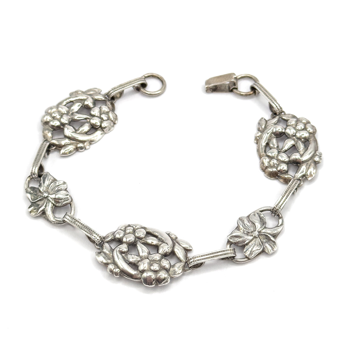 Overhead view of the whole bracelet opened into a horseshoe, the hook and round ring parted at the top, so all five floral stations and the ribbed connecting bars sit flat in one sweep.
