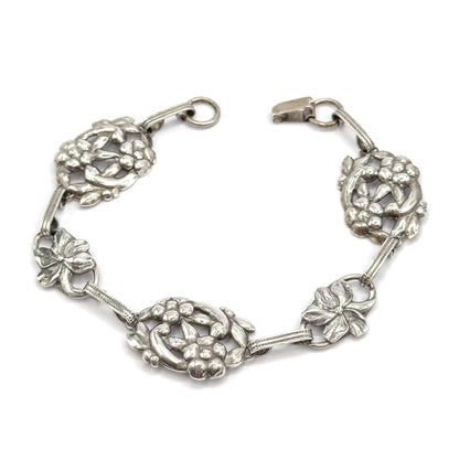 Overhead view of the whole bracelet opened into a horseshoe, the hook and round ring parted at the top, so all five floral stations and the ribbed connecting bars sit flat in one sweep.