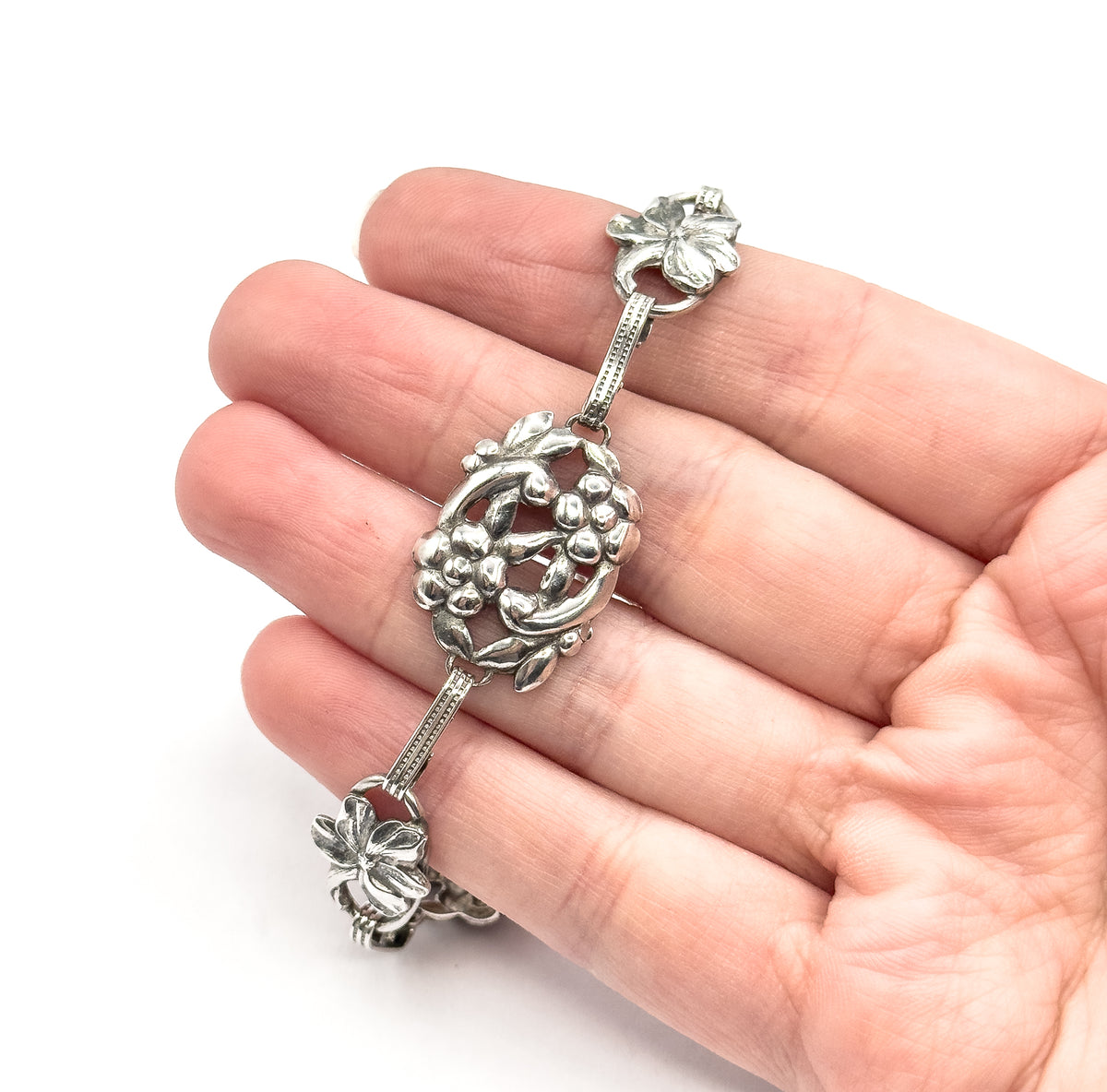 Mid-century openwork floral sterling silver bracelet laid across an open palm, its oval flower station and smaller leaf links spanning the fingers, with patina deep in the recesses.