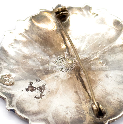 The reverse of the brooch in close-up, showing the scalloped sterling silver back with its long pin stem crossing to the clasp and small stamped marks near the centre.