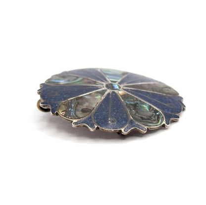 Low edge-on view across the face on white, the scalloped sterling silver rim in profile with the pin hinge just visible at the left side and the central silver boss catching light.