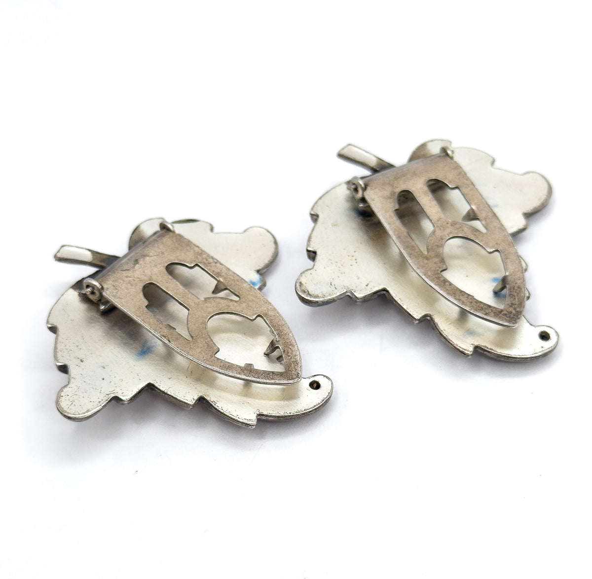 Angled from the side, the backs show the pierced shield-shaped plates standing proud of the leaf outlines with the hinged clip blades lifted away from the metal.