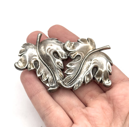 The pair rests face-up in an open palm, showing size against the fingers, with the sculptural overlapping leaves and veined centres catching light under a soft patina.