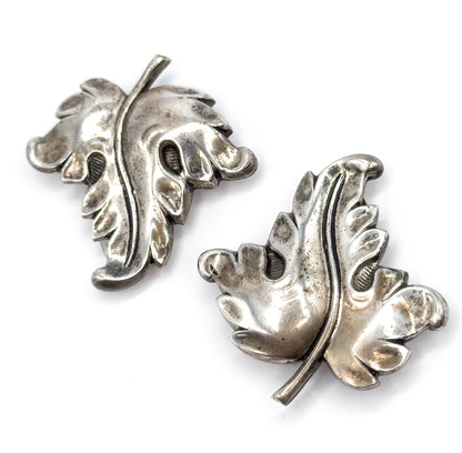 Both clips shown face-up on white, turned in opposite directions so each full leaf outline is visible, with the raised central rib running stem to tip and patina darkening the slot openings.