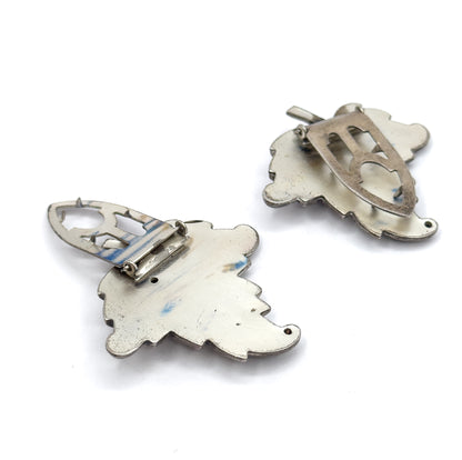 A matched pair of leaf dress clips in silver plate, shown back-up on a white background so the cut-out clip mechanisms and scalloped leaf outlines are visible.