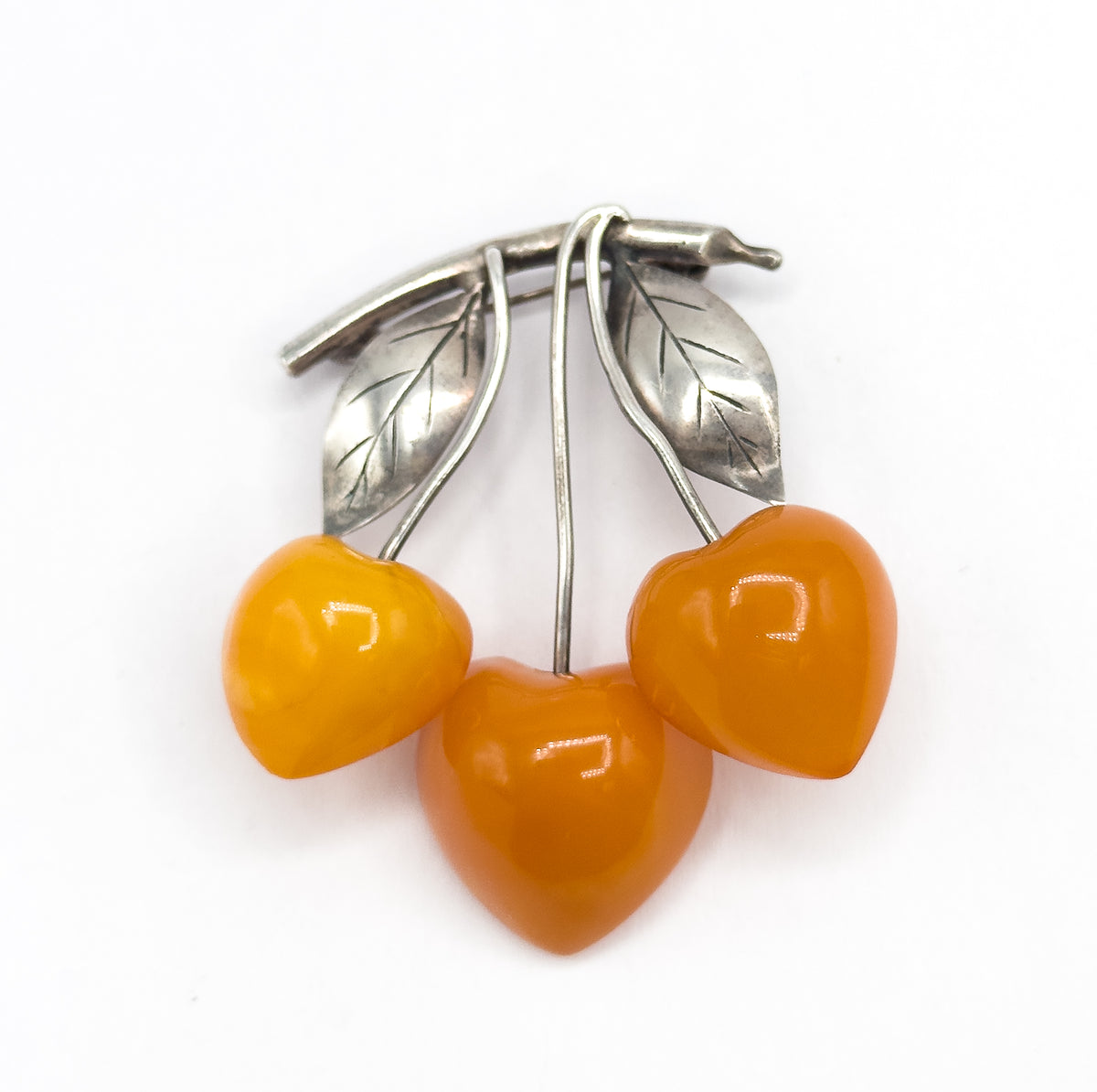Straight-on flat view on white, the three polished apricot amber cherries side by side below and the two veined silver leaves with curving stems arching above them.