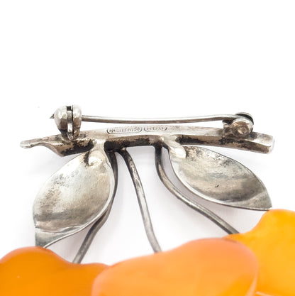Close view of the reverse, where the hinged pin stem spans a silver bar bearing small impressed stamps, with the stems, leaves and an apricot amber drop below.