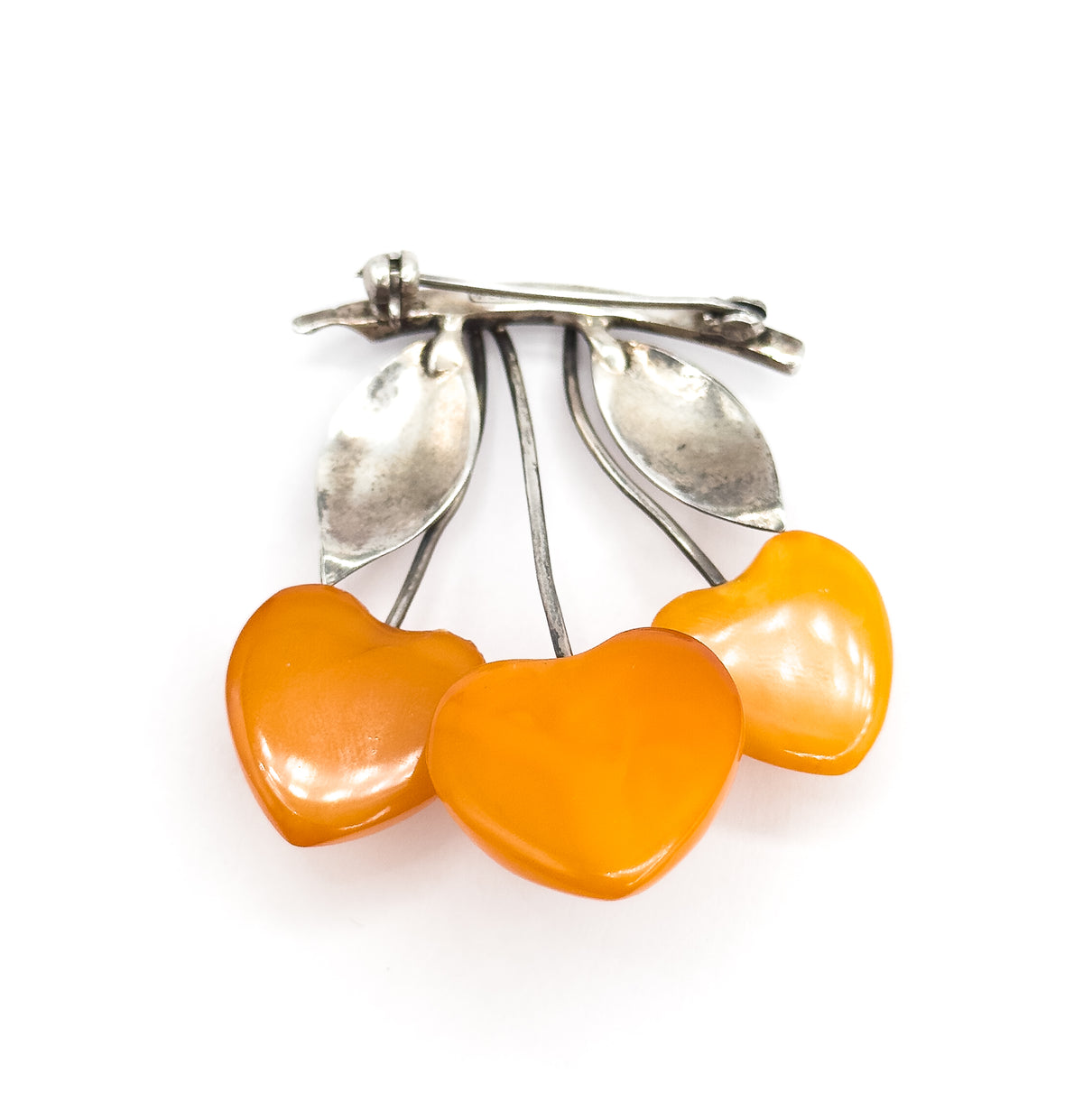Tilted view from below the pin, the three heart-shaped apricot amber cherries filling the foreground while the silver stems, two leaves and the straight pin stem recede behind.