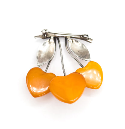 Tilted view from below the pin, the three heart-shaped apricot amber cherries filling the foreground while the silver stems, two leaves and the straight pin stem recede behind.