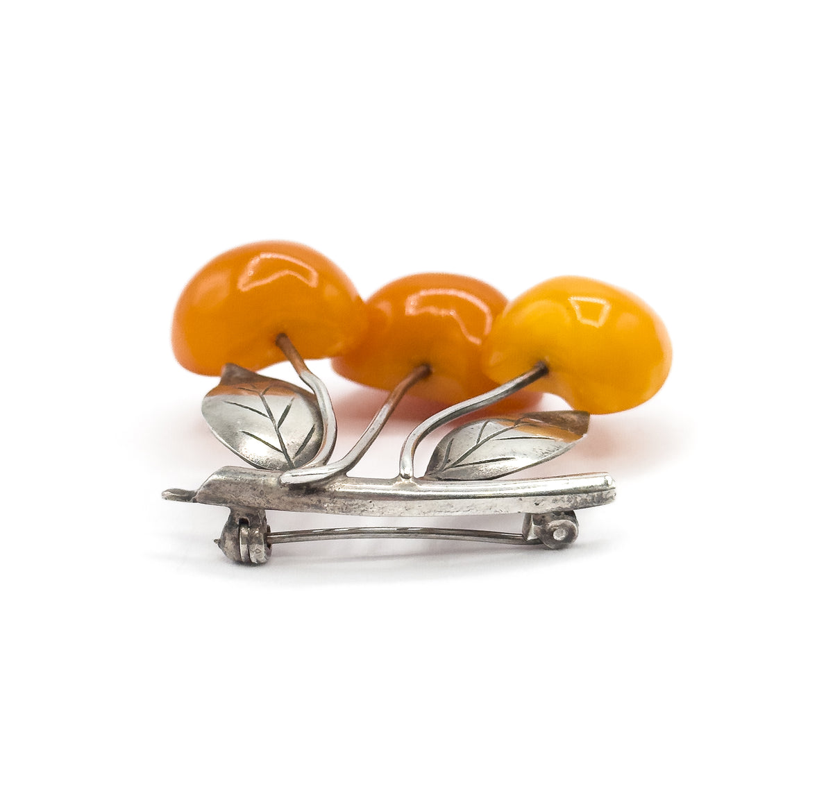 Edge-on view from the front, the three apricot amber cherries rising above the silver bar whose full length shows the hinge at one end and rounded catch at the other, pin stem drawn across.