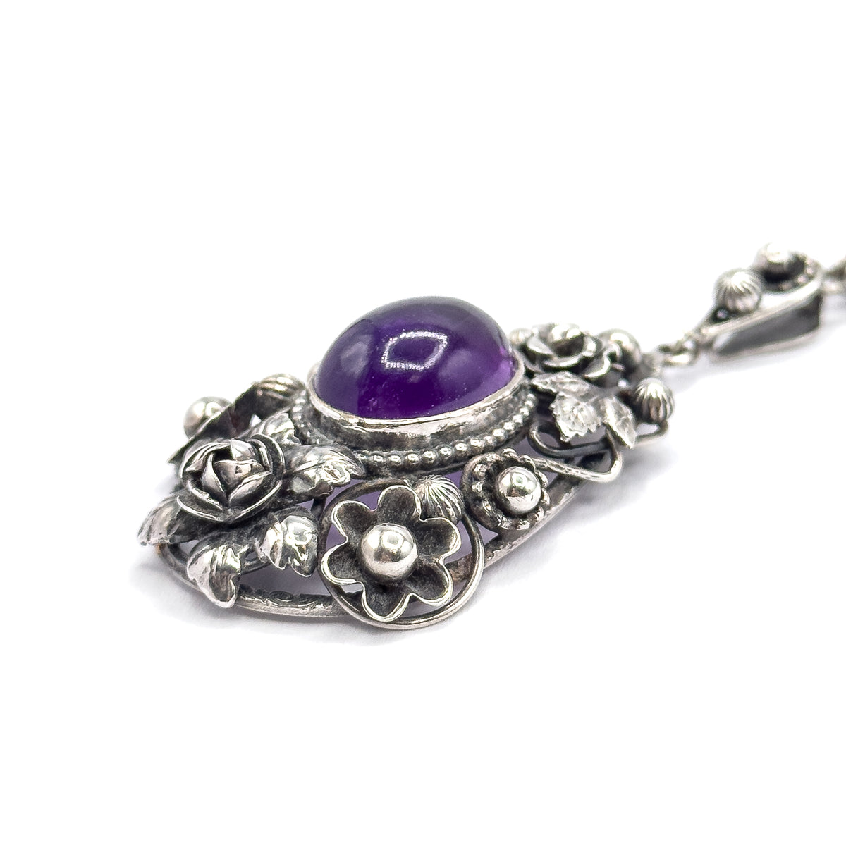 Tilted view from the lower edge, bringing the gallery's five-petalled flower and silver bead forward, the amethyst dome above it and the bail with its blossom angled away to the upper right.