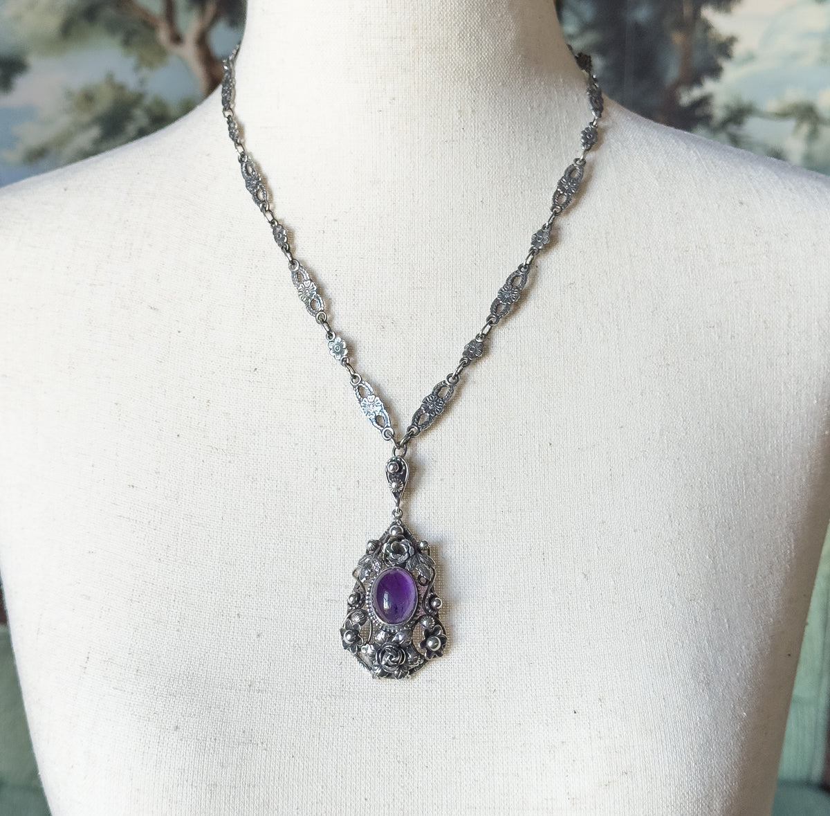 Full length view at the neck, the sterling silver chain of small floral and oval links running down both sides to a linked drop above the amethyst pendant.