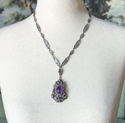 Full length view at the neck, the sterling silver chain of small floral and oval links running down both sides to a linked drop above the amethyst pendant.