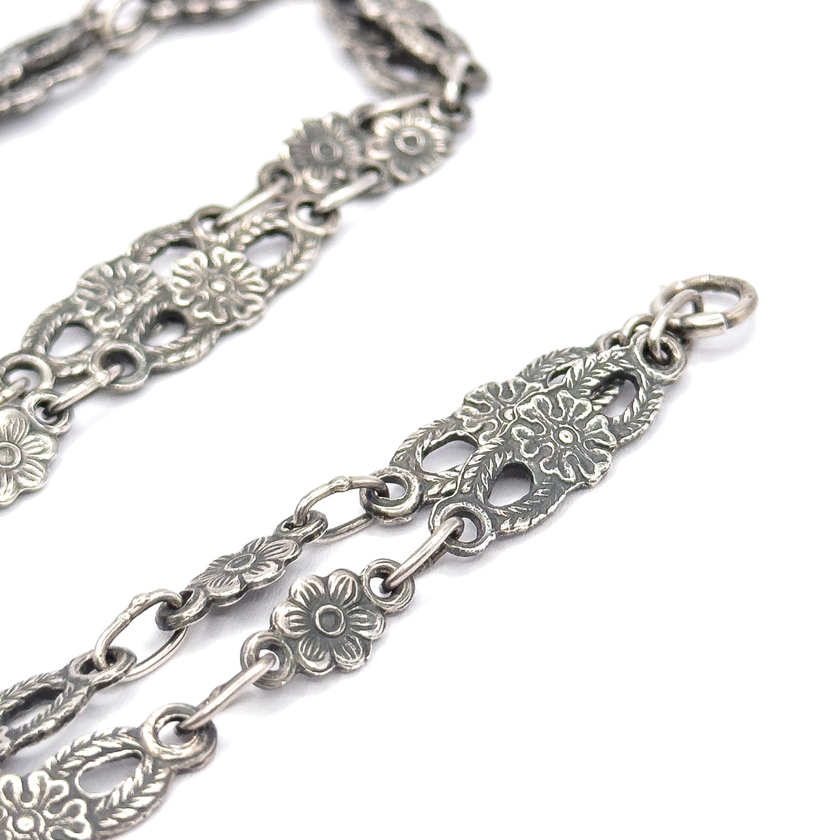 Close view of the sterling silver chain alone, its pierced oval panels of flowers and leaves alternating with small round blossom links and plain connecting rings, ending at a jump ring.