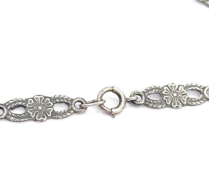 Close view of the round spring-ring clasp with its sliding tab, linked by small jump rings between two pierced floral chain panels, patina darkening the recesses.