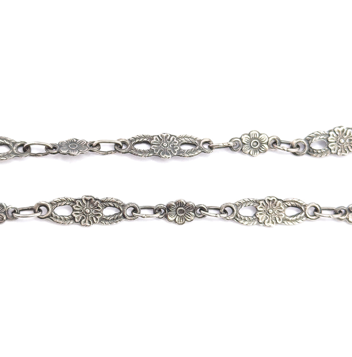 Two parallel runs of the sterling silver chain side by side, showing both faces of the pierced oval panels and round blossom links with patina deep in the recesses.