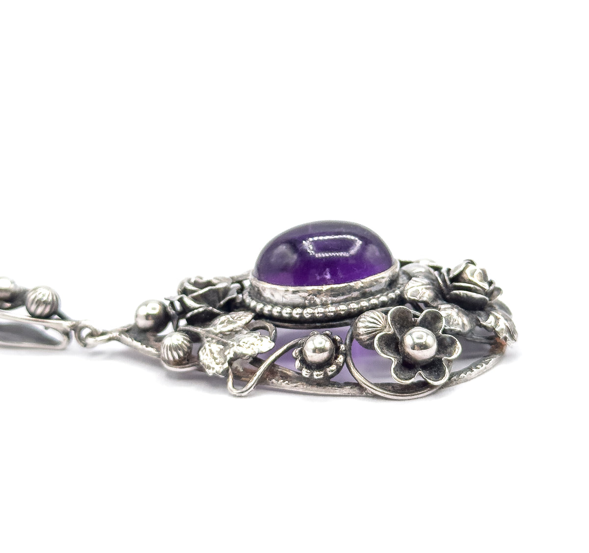 Steep side angle across the pendant, showing the amethyst standing high in its beaded bezel above sterling silver flowers, leaves and berries, with the bail at the left.