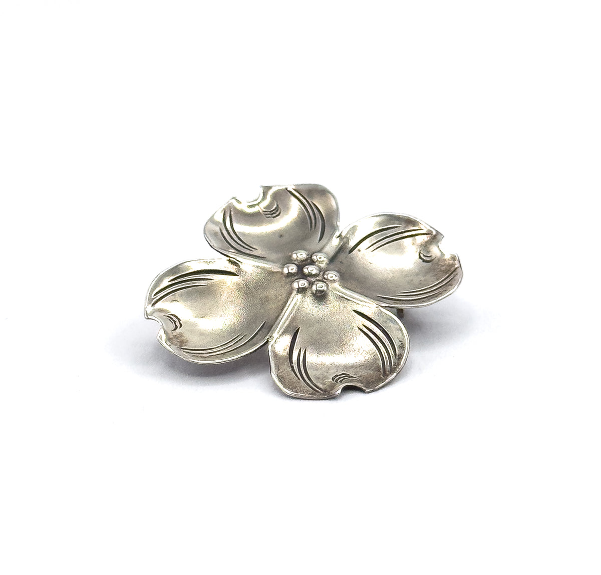 Front view from slightly above, showing all four petals spread flat with their notched tips and the small cluster of beads at the centre, patina settling into the etched veins.