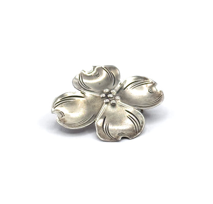 Front view from slightly above, showing all four petals spread flat with their notched tips and the small cluster of beads at the centre, patina settling into the etched veins.