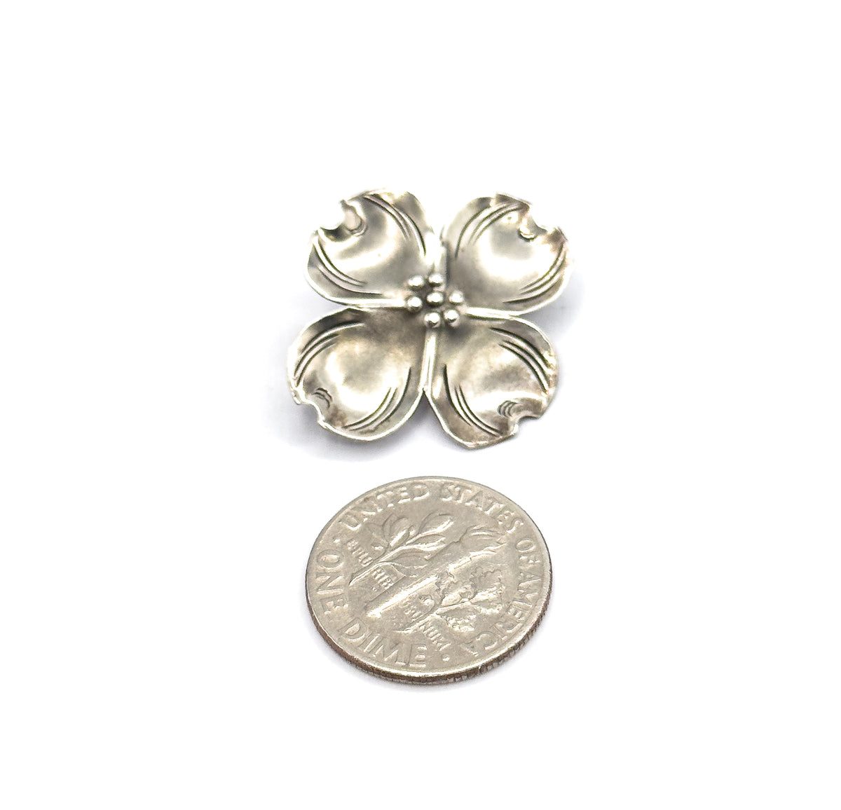 Vintage Stuart Nye sterling silver dogwood flower brooch, shown face-up on white beside a dime for scale, its four veined petals meeting at a cluster of small beads.