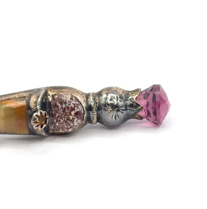 Close-up of the thistle head end, where a faceted purple paste stone sits in a pointed engraved cap, with a small star-set golden paste accent on the banded agate below.
