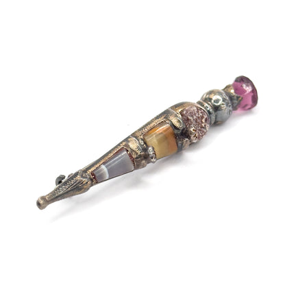 Full-length diagonal view from the front, the pointed silver tip and projecting pin stem at the lower left, banded agate and onyx panels rising to the purple paste at the thistle head.