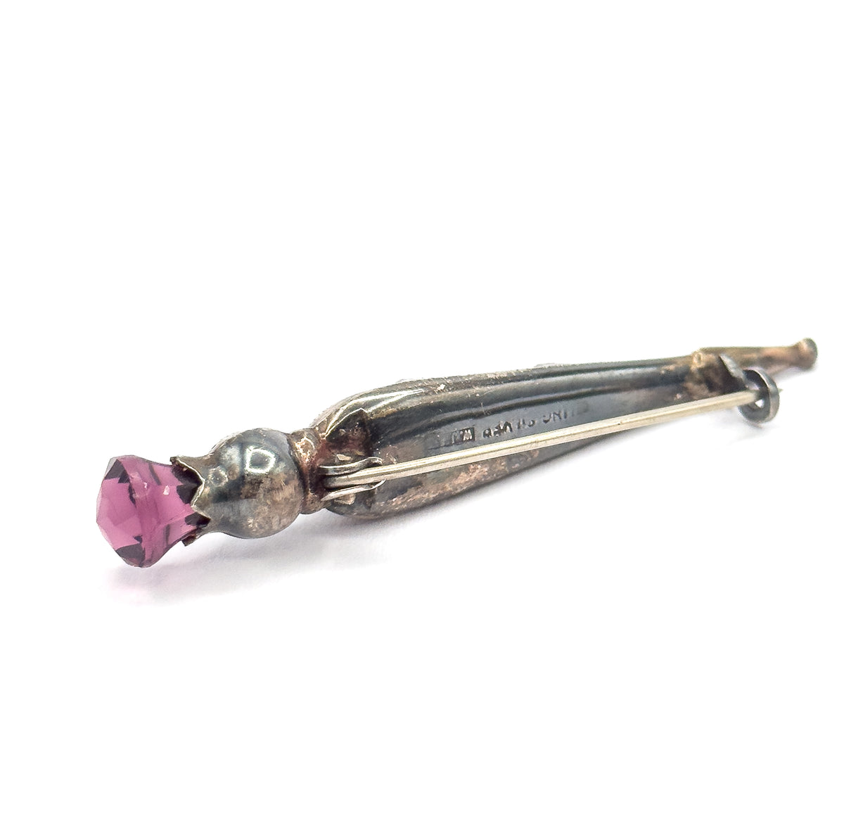 Angled back view with the faceted purple paste stone at lower left, the pin stem running the length of the body past a partially visible makers mark to the catch and hinge at upper right.