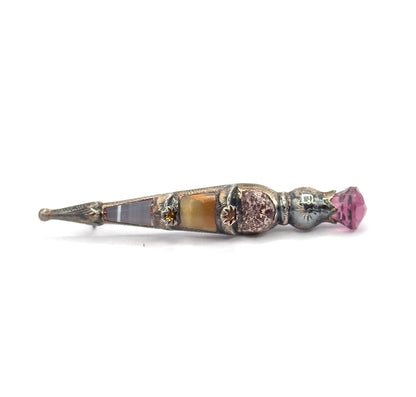 Low, nearly level side-on view with the pointed engraved tip at far left, the banded agate and onyx panels running in a line past two star-set golden paste accents to the faceted purple paste at right.