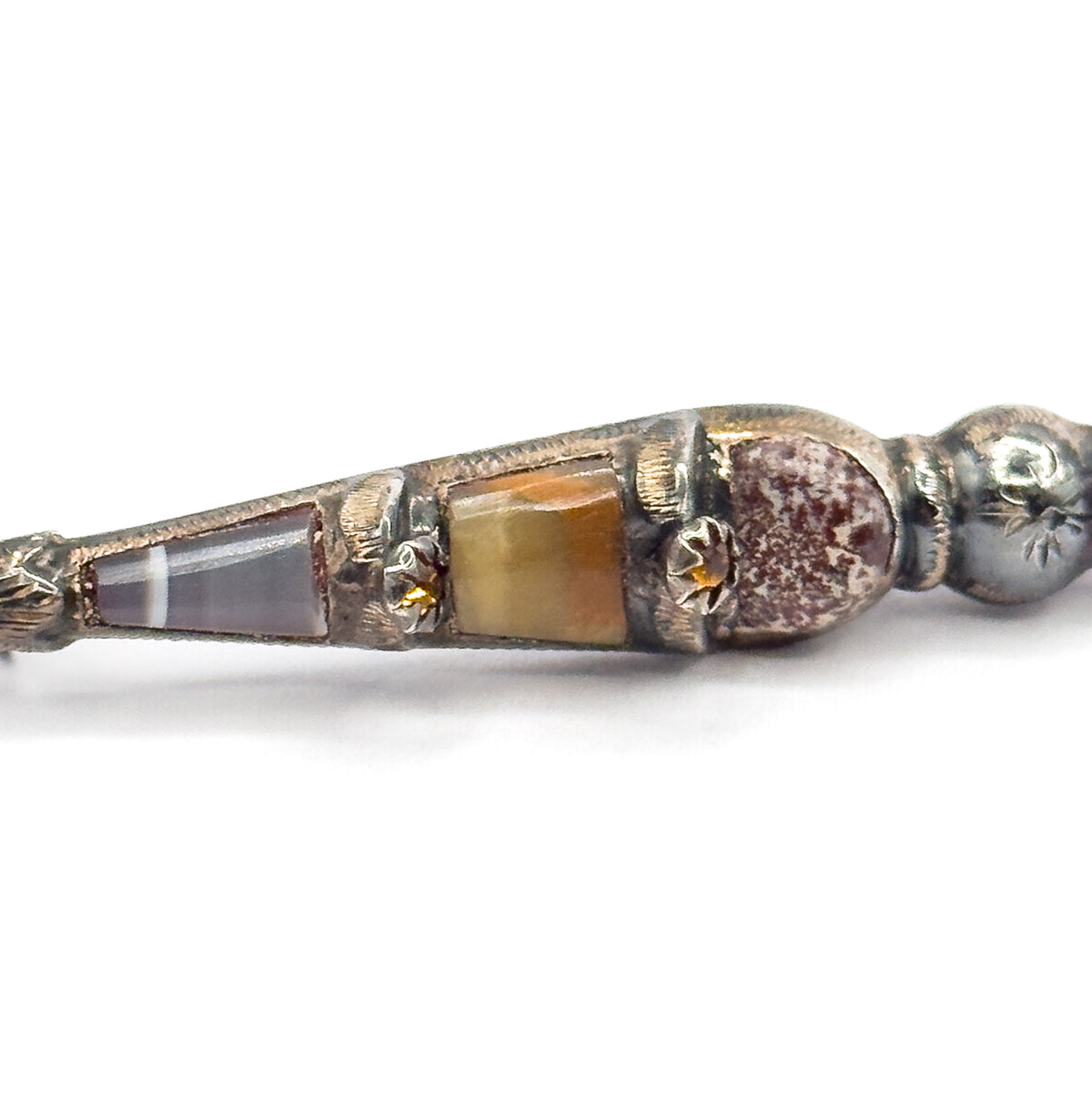Victorian Scottish thistle brooch in sterling silver, shown in close-up at an angle on a white background, its tapering body set with banded agate and onyx panels between engraved collars.