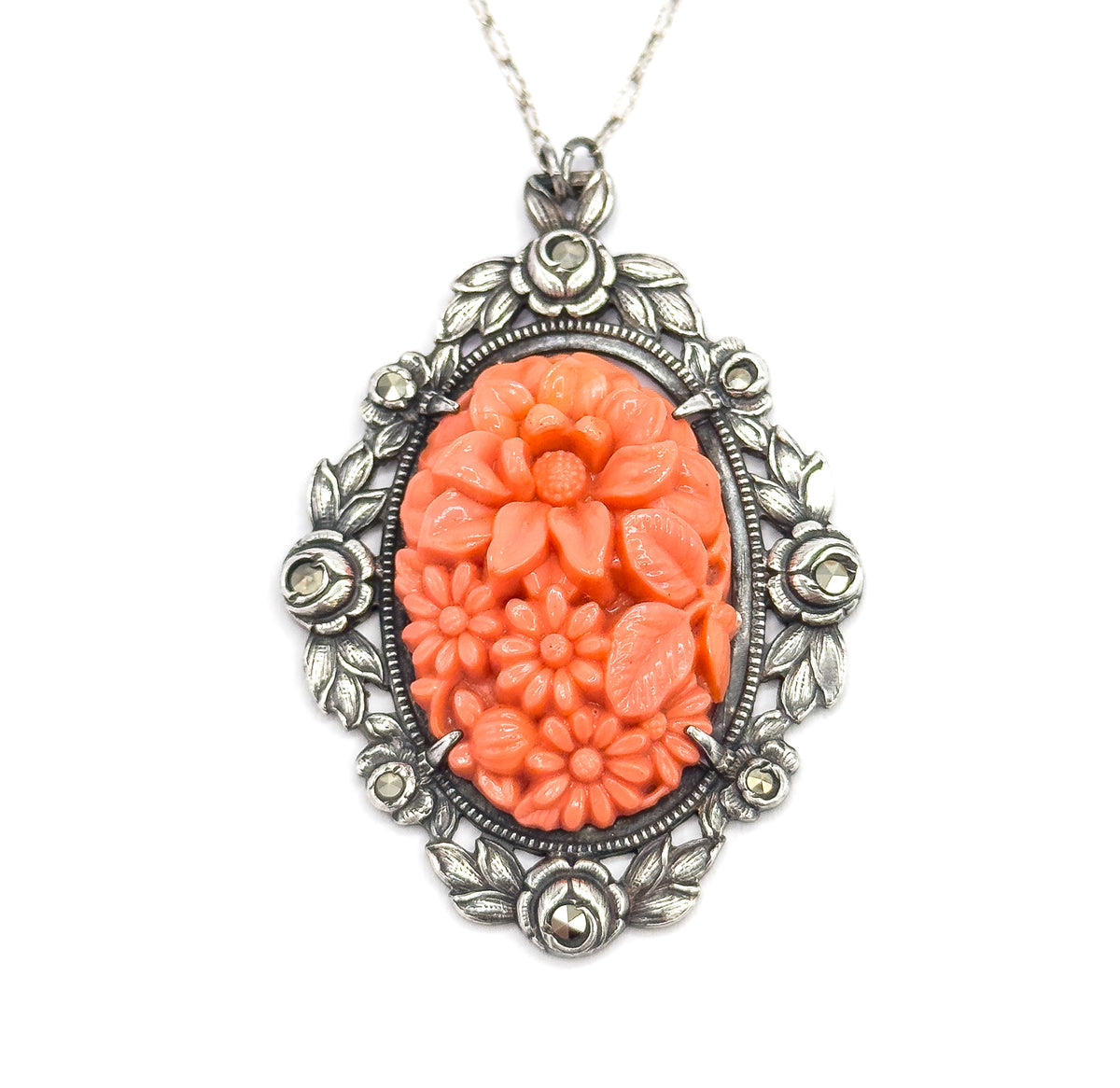 Hanging upright from its chain, the pendant squarely face-on so the four silver roses with marcasite centres, leafy frame and molded coral-coloured glass flowers are all seen at once.