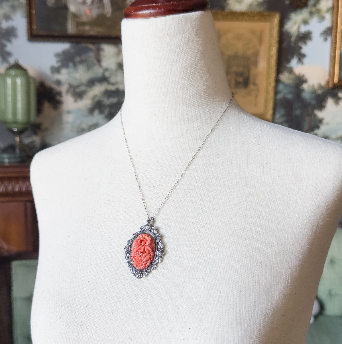 Angled three-quarter view at the neck, showing the full drape of the fine chain over the shoulder and the molded floral coral-coloured glass centre within its marcasite-set frame.