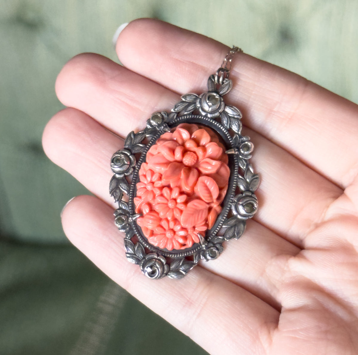 Shown resting across open fingers, which give a sense of its size: the molded floral coral-coloured glass centre sits in a sterling silver frame of leaves and marcasite-set flower forms.